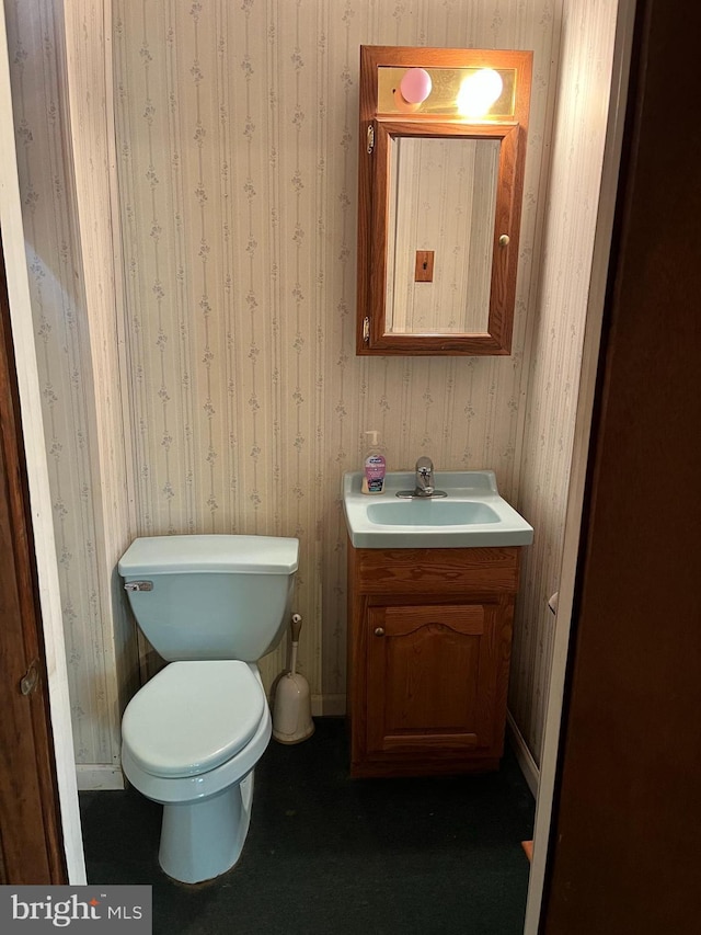 half bathroom featuring wallpapered walls, toilet, vanity, and baseboards