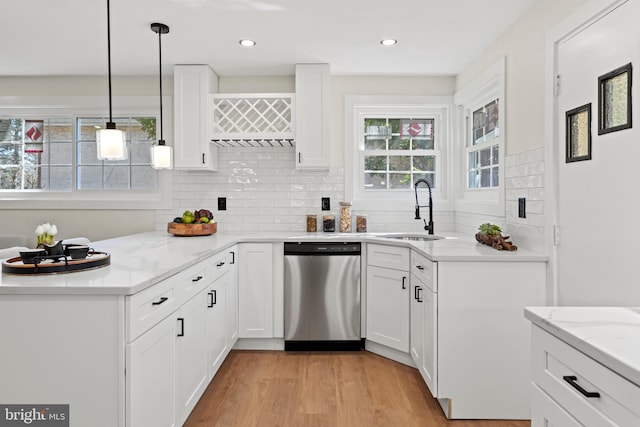 kitchen with light stone countertops, light wood-style flooring, stainless steel dishwasher, white cabinetry, and a sink