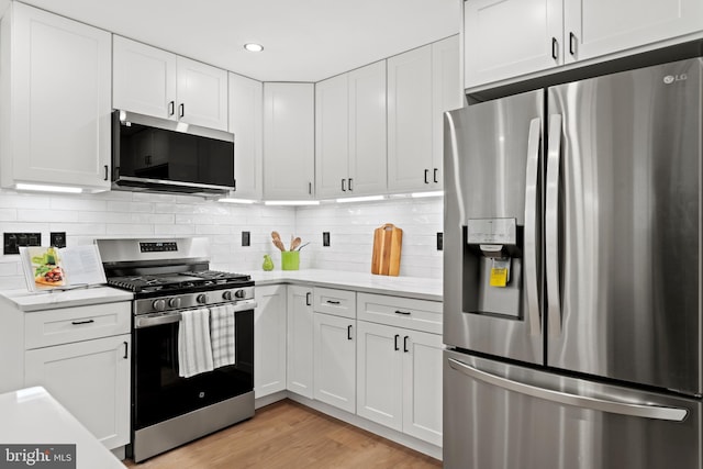 kitchen with light wood finished floors, white cabinets, backsplash, and appliances with stainless steel finishes