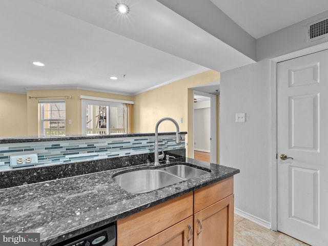 kitchen featuring dark stone counters, decorative backsplash, dishwashing machine, light tile patterned flooring, and a sink