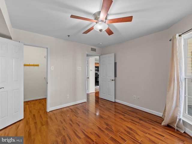 unfurnished bedroom with ceiling fan, a walk in closet, baseboards, and wood finished floors