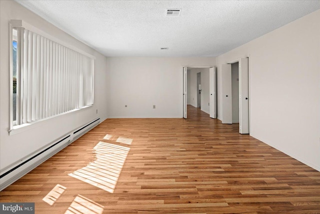 unfurnished room featuring visible vents, baseboards, light wood-type flooring, baseboard heating, and a textured ceiling