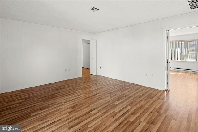 unfurnished room featuring visible vents, wood finished floors, and a baseboard radiator