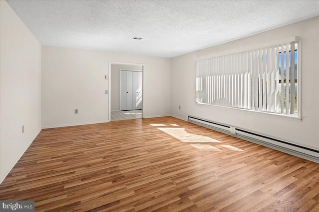 empty room with a wealth of natural light, a baseboard radiator, a textured ceiling, and wood finished floors