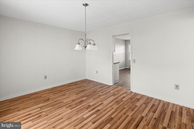 unfurnished room with a chandelier, a textured ceiling, baseboards, and wood finished floors