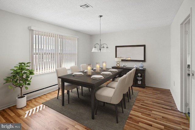 dining space featuring visible vents, a chandelier, baseboard heating, wood finished floors, and a textured ceiling