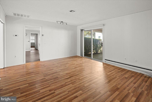 interior space featuring a baseboard heating unit, wood finished floors, visible vents, and a textured ceiling