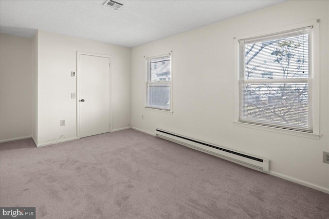 unfurnished room with a baseboard heating unit, plenty of natural light, visible vents, and carpet floors