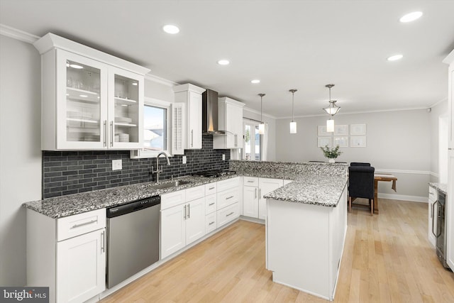 kitchen with a peninsula, stainless steel appliances, wall chimney range hood, and ornamental molding