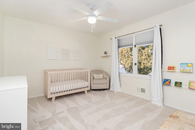 bedroom with visible vents, a crib, baseboards, carpet flooring, and a ceiling fan