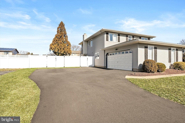 view of property exterior with an attached garage, fence, a lawn, a chimney, and driveway