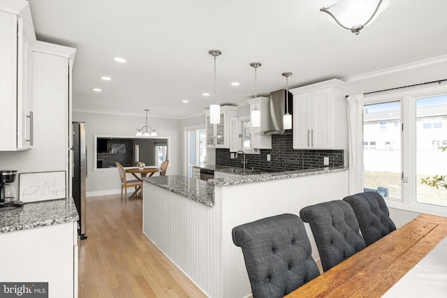 kitchen featuring stainless steel appliances, white cabinetry, crown molding, wall chimney range hood, and backsplash