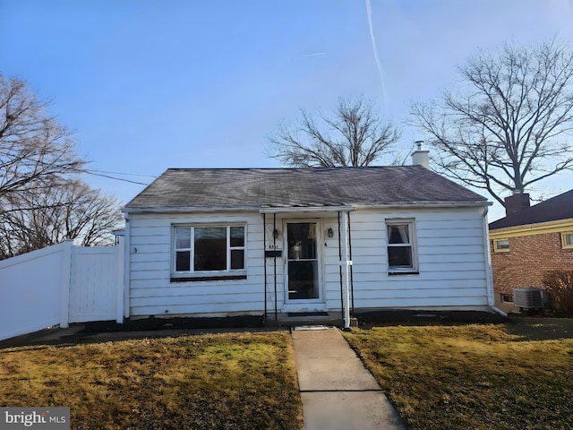 bungalow-style house with a front lawn, cooling unit, fence, and a chimney