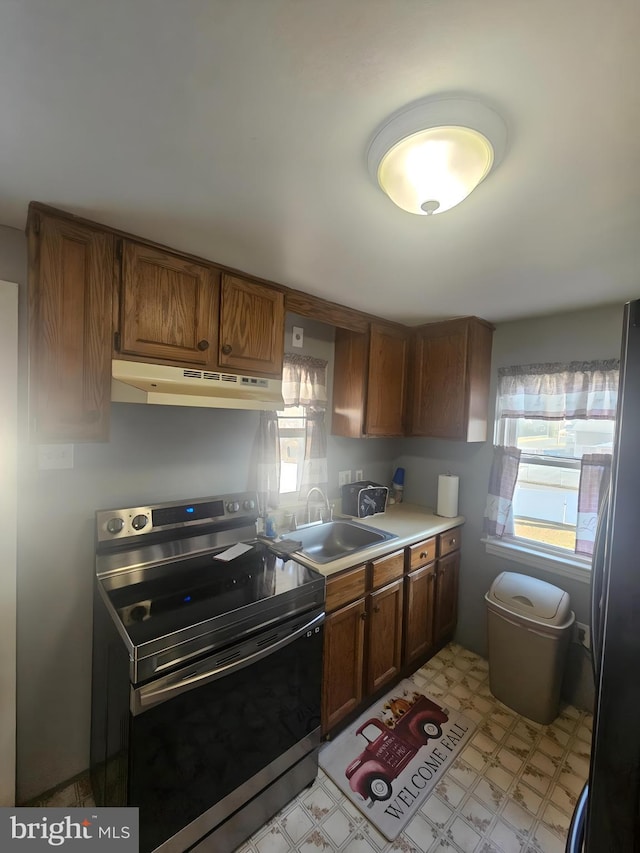 kitchen with under cabinet range hood, light floors, brown cabinets, stainless steel appliances, and a sink