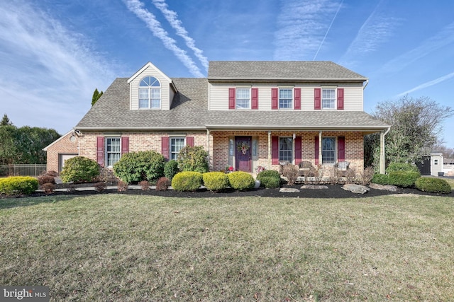 view of front of house featuring a front lawn, covered porch, brick siding, and roof with shingles