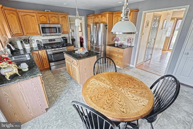 kitchen with a kitchen island, a sink, stainless steel appliances, decorative light fixtures, and backsplash