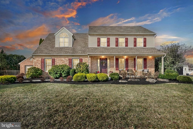 view of front of home with brick siding, covered porch, a front yard, and a shingled roof