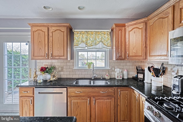 kitchen with a sink, backsplash, appliances with stainless steel finishes, and dark stone countertops