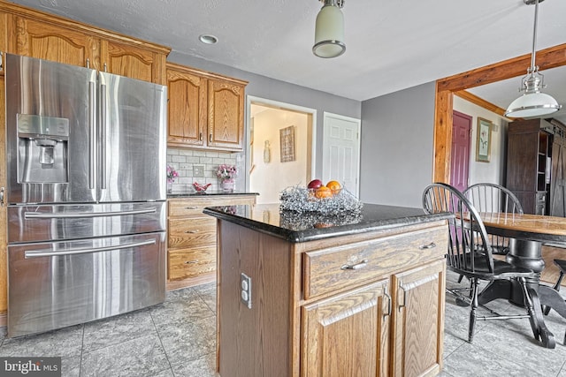 kitchen with a kitchen island, decorative backsplash, dark stone countertops, hanging light fixtures, and stainless steel fridge