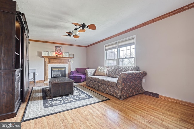 living area featuring visible vents, light wood finished floors, ceiling fan, ornamental molding, and a glass covered fireplace