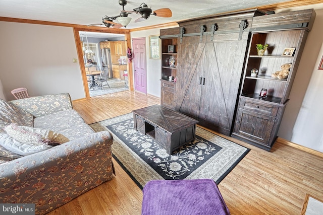 living area with ceiling fan, a barn door, wood finished floors, and ornamental molding