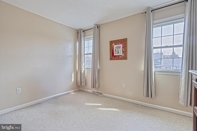 carpeted spare room with a wealth of natural light, visible vents, and baseboards