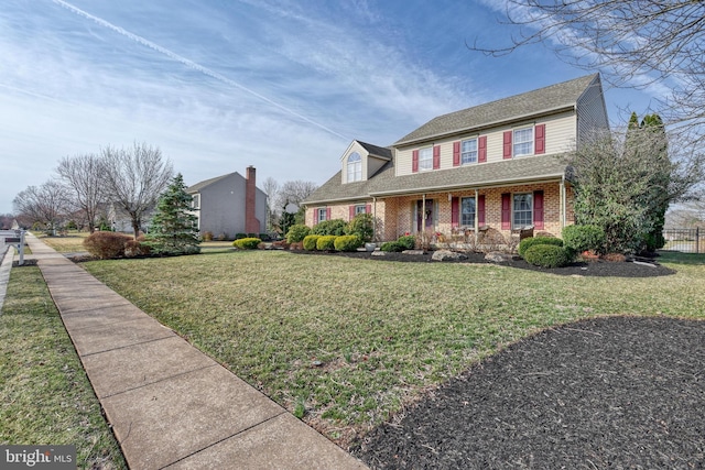 view of front facade featuring brick siding, a porch, a front lawn, and fence