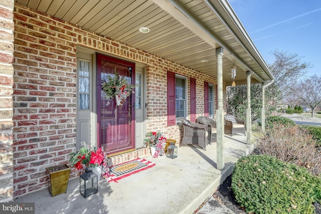 view of exterior entry featuring brick siding and a porch