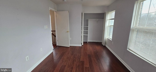 unfurnished bedroom with a closet, baseboards, multiple windows, and wood finished floors