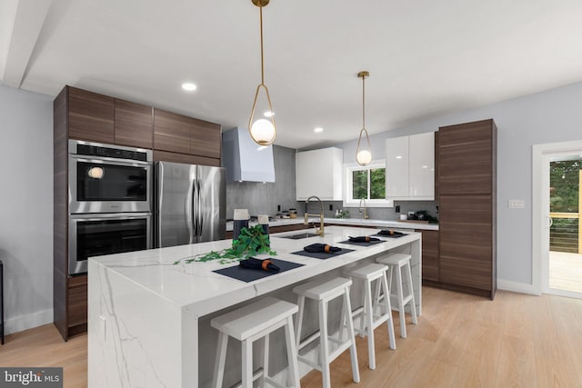 kitchen with modern cabinets, a sink, stainless steel appliances, light wood finished floors, and decorative backsplash