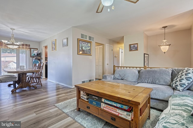 living room with ceiling fan with notable chandelier, wood finished floors, and baseboards