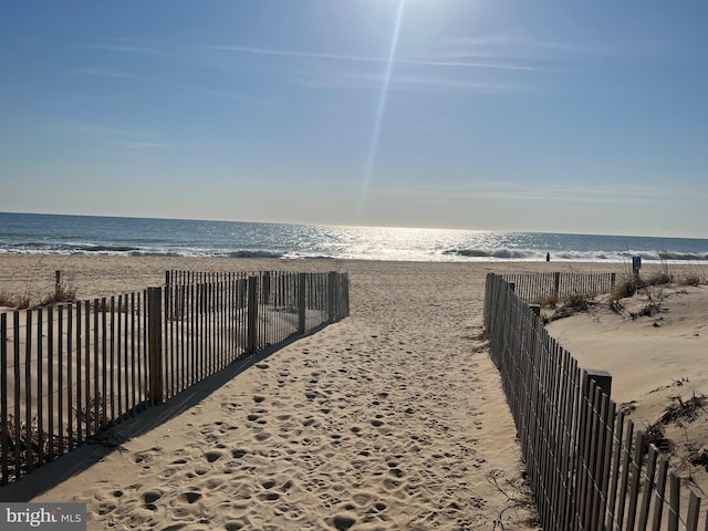 surrounding community with a view of the beach, fence, and a water view