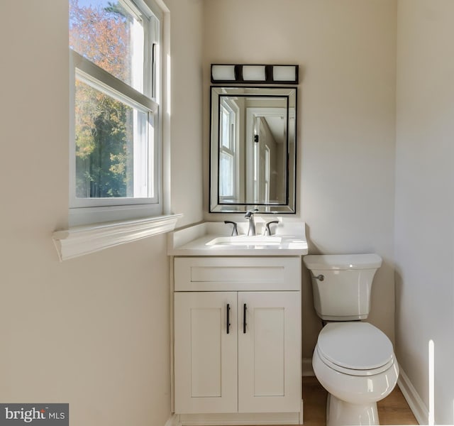 half bath featuring toilet, vanity, baseboards, and wood finished floors