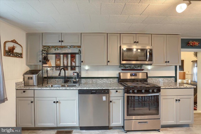 kitchen featuring gray cabinets, appliances with stainless steel finishes, light stone countertops, and a sink