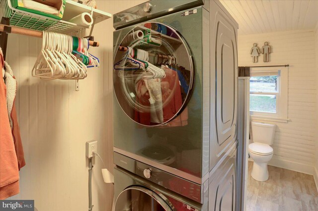 washroom with baseboards, stacked washer and dryer, wood finished floors, and laundry area