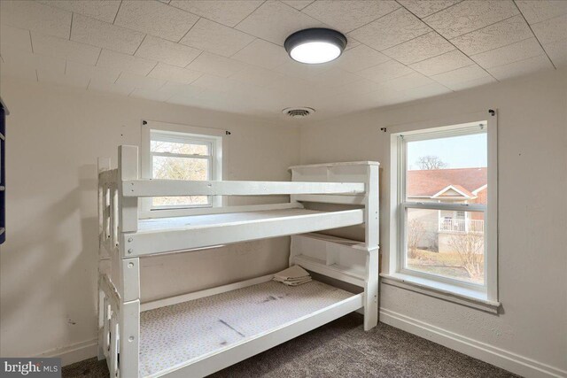 unfurnished bedroom featuring carpet flooring, multiple windows, visible vents, and baseboards