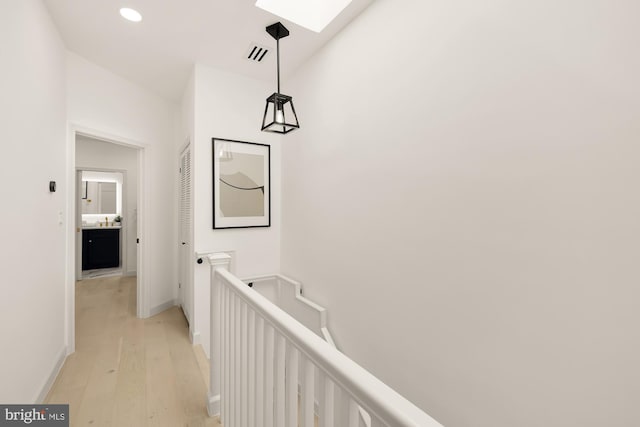 hallway featuring light wood finished floors, visible vents, baseboards, an upstairs landing, and a skylight