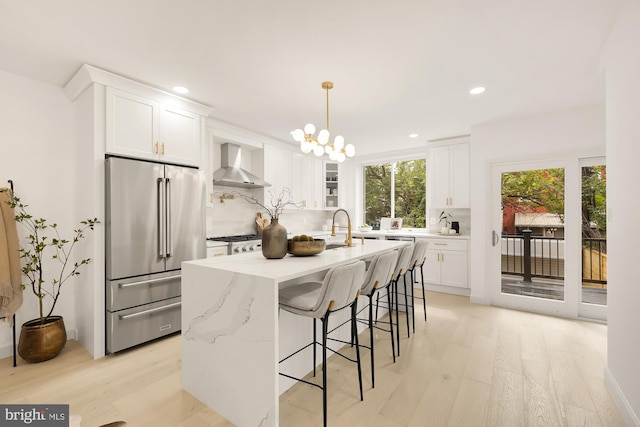 kitchen featuring wall chimney range hood, white cabinets, light wood finished floors, decorative backsplash, and high end refrigerator