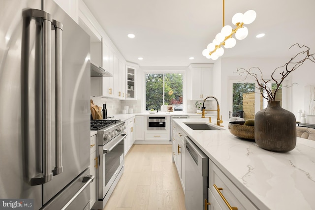 kitchen with a sink, premium appliances, light stone counters, tasteful backsplash, and light wood finished floors