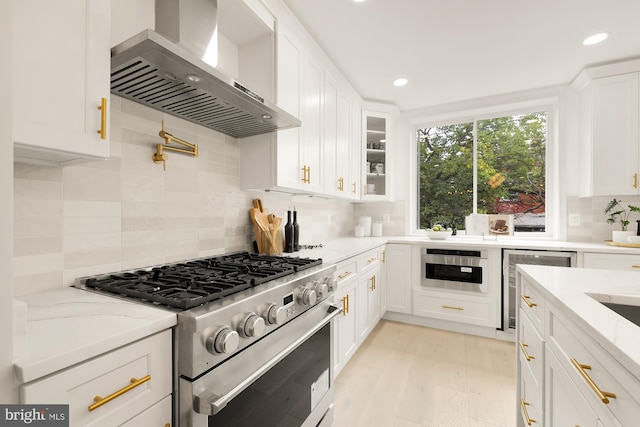 kitchen with glass insert cabinets, light stone counters, appliances with stainless steel finishes, white cabinets, and wall chimney exhaust hood