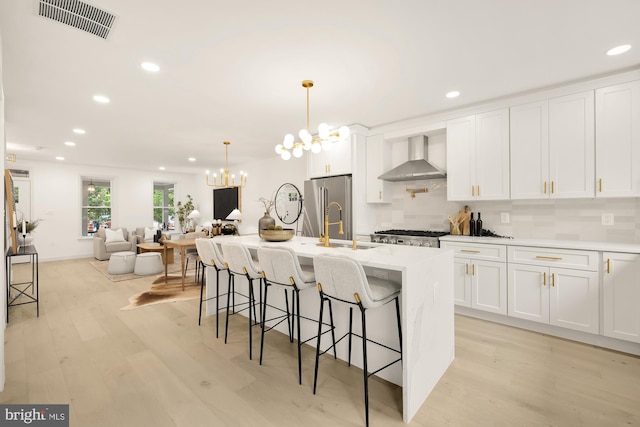 kitchen featuring light wood finished floors, visible vents, wall chimney range hood, white cabinets, and high end fridge