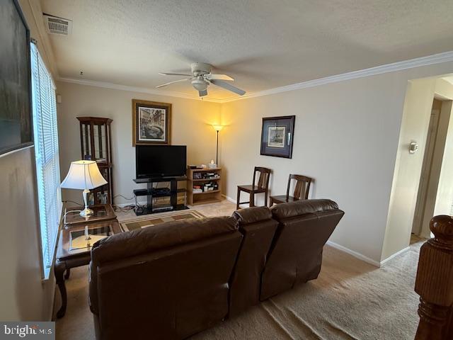 living area featuring visible vents, crown molding, baseboards, carpet floors, and a ceiling fan