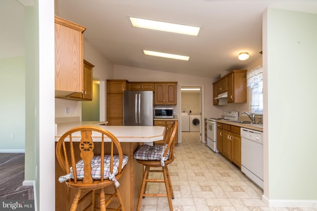 kitchen with a peninsula, light countertops, appliances with stainless steel finishes, a kitchen breakfast bar, and washer and clothes dryer