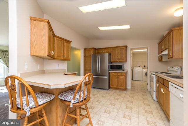 kitchen featuring a peninsula, appliances with stainless steel finishes, under cabinet range hood, a kitchen breakfast bar, and independent washer and dryer