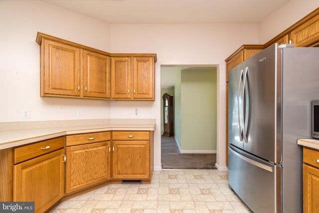 kitchen with baseboards, brown cabinets, light countertops, and freestanding refrigerator