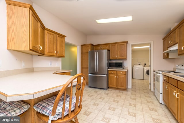 kitchen with a peninsula, under cabinet range hood, appliances with stainless steel finishes, a kitchen breakfast bar, and independent washer and dryer