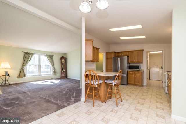 kitchen with a breakfast bar, washer / clothes dryer, stainless steel appliances, vaulted ceiling, and light countertops