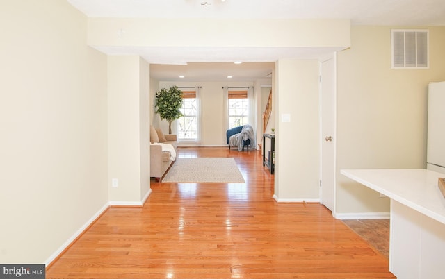 hall featuring visible vents, baseboards, and light wood-style flooring