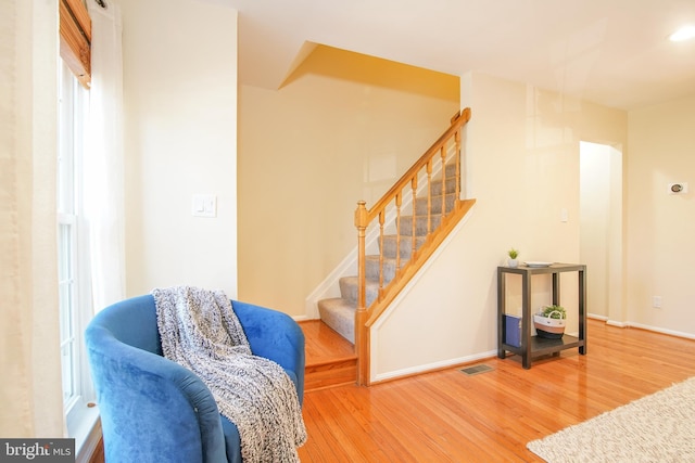 living area with stairway, wood finished floors, visible vents, and baseboards