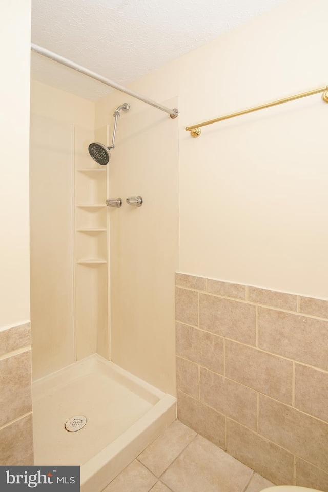 bathroom with a textured ceiling, tile walls, a shower stall, and tile patterned flooring